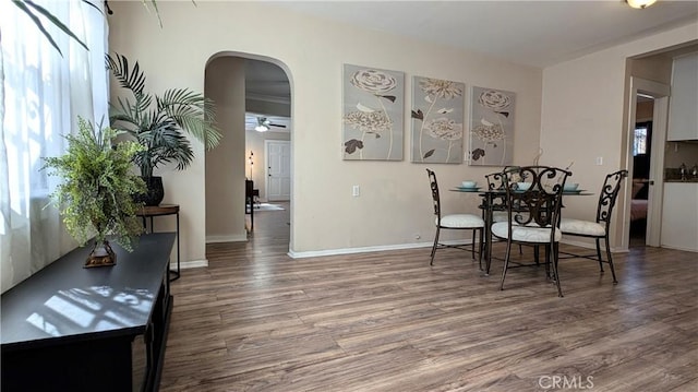 dining room with arched walkways, plenty of natural light, baseboards, and wood finished floors