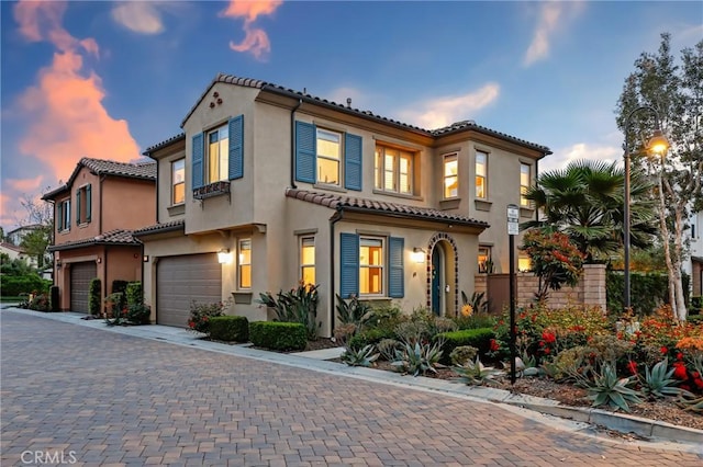 mediterranean / spanish-style home featuring a tiled roof, decorative driveway, stucco siding, and a garage