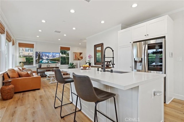 kitchen with a sink, stainless steel fridge with ice dispenser, recessed lighting, a kitchen bar, and ornamental molding