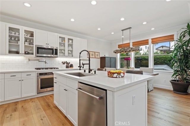 kitchen featuring appliances with stainless steel finishes, a sink, light countertops, ornamental molding, and an island with sink