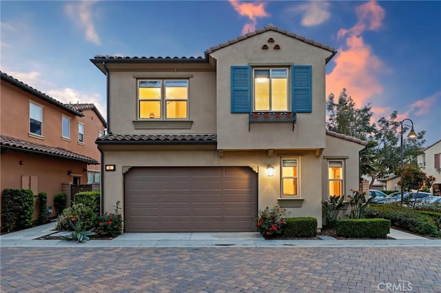 mediterranean / spanish-style home featuring an attached garage, driveway, a tile roof, and stucco siding