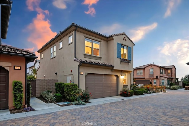 mediterranean / spanish house featuring fence, stucco siding, an attached garage, and a tile roof