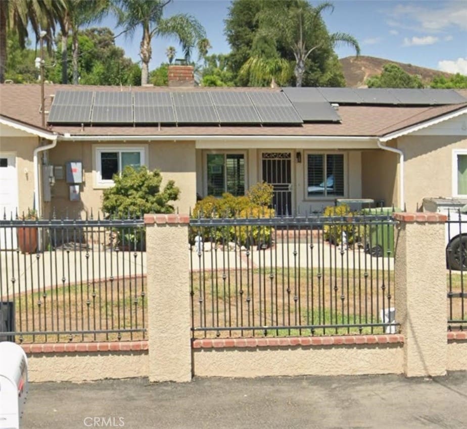exterior space featuring a fenced front yard, stucco siding, a chimney, and solar panels
