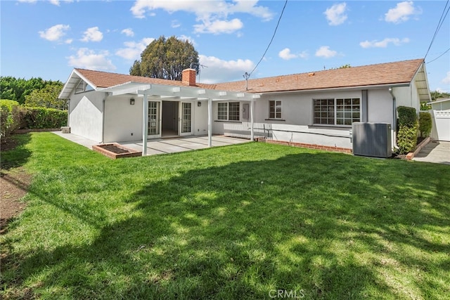 rear view of house featuring central AC, stucco siding, a chimney, a lawn, and a patio