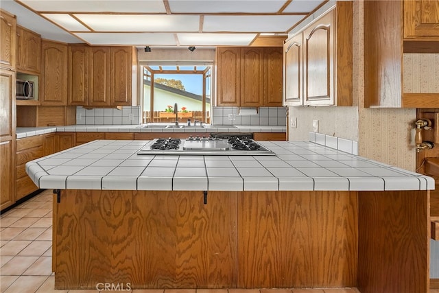 kitchen with brown cabinetry, a sink, stainless steel microwave, and stovetop