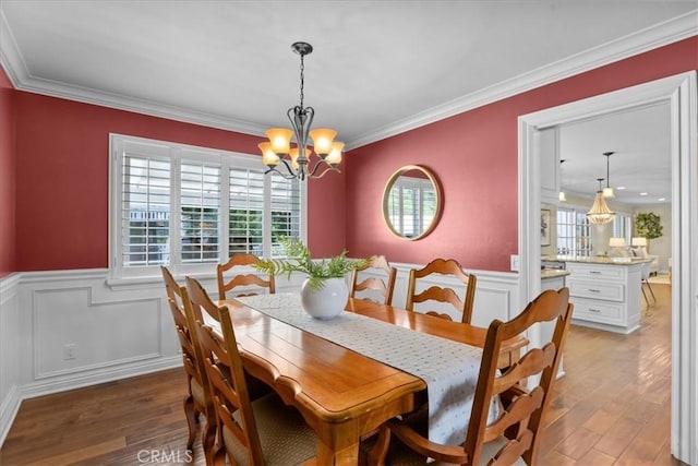 dining room featuring crown molding, a notable chandelier, a decorative wall, light wood-style flooring, and a wainscoted wall