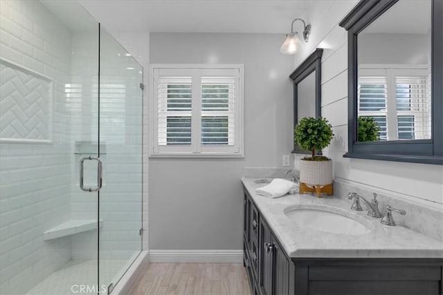 bathroom with double vanity, a shower stall, wood finished floors, a sink, and baseboards