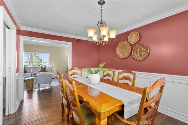 dining room featuring an inviting chandelier, crown molding, wood finished floors, and a wainscoted wall
