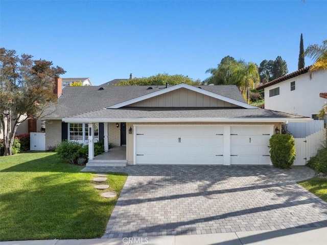 single story home featuring a front lawn, fence, decorative driveway, a shingled roof, and an attached garage