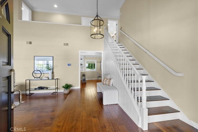 stairs with a high ceiling, a notable chandelier, wood finished floors, and visible vents