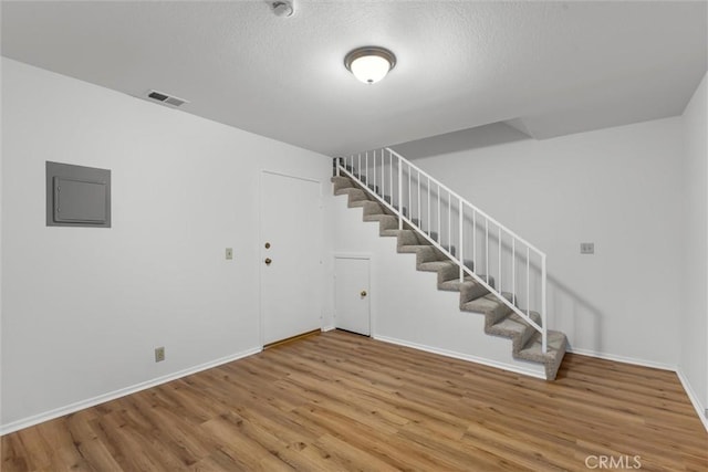 finished below grade area with visible vents, wood finished floors, baseboards, stairway, and electric panel