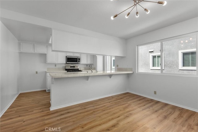 kitchen with an inviting chandelier, tile counters, white cabinetry, light wood finished floors, and appliances with stainless steel finishes