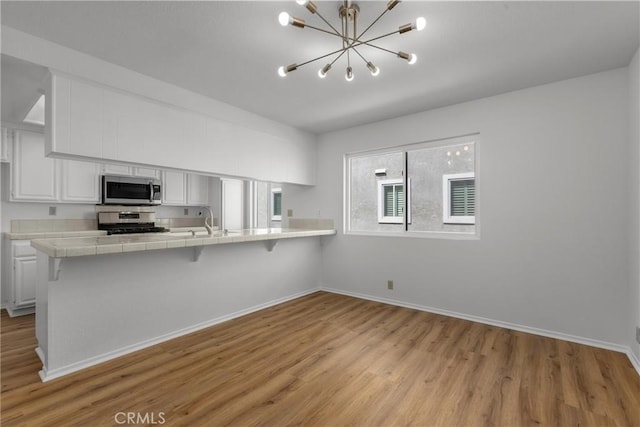 kitchen with white cabinets, a notable chandelier, tile counters, stainless steel appliances, and light wood-type flooring