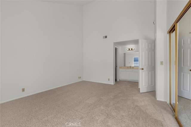 unfurnished bedroom with baseboards, a high ceiling, and light carpet