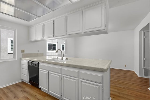 kitchen featuring light wood-type flooring, a sink, white cabinets, a peninsula, and black dishwasher
