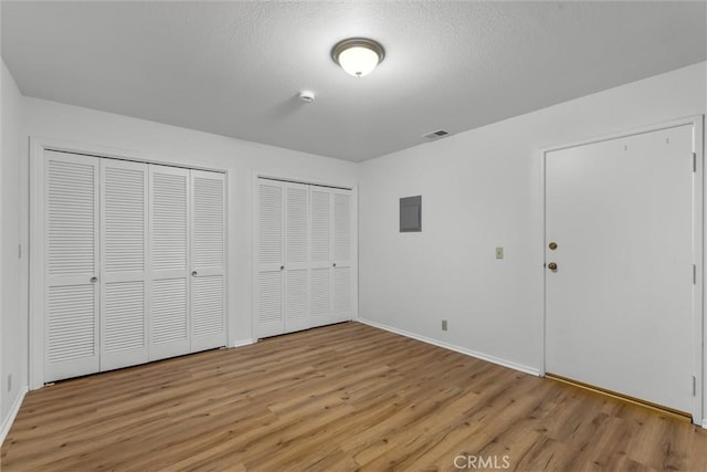 unfurnished bedroom with two closets, baseboards, visible vents, and light wood-style floors