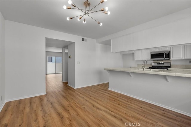kitchen with an inviting chandelier, light wood-style floors, tile counters, stainless steel appliances, and baseboards