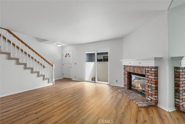 unfurnished living room with baseboards, wood finished floors, a fireplace, and stairway