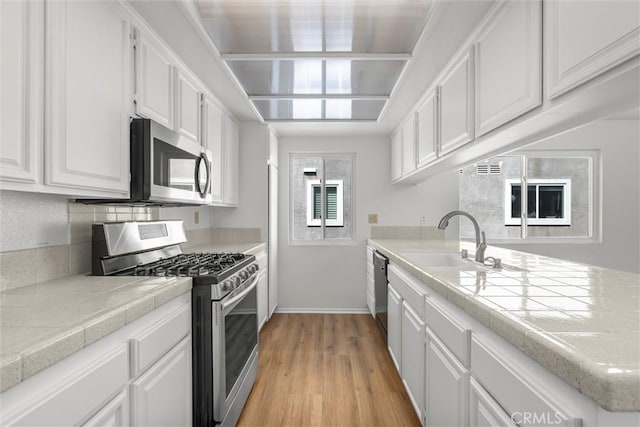 kitchen with a peninsula, white cabinetry, a sink, light wood-style flooring, and stainless steel appliances