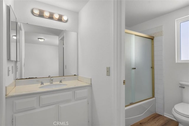 bathroom featuring vanity, enclosed tub / shower combo, wood finished floors, and toilet