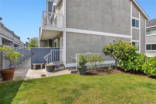 back of house featuring a lawn, fence, stucco siding, and a balcony