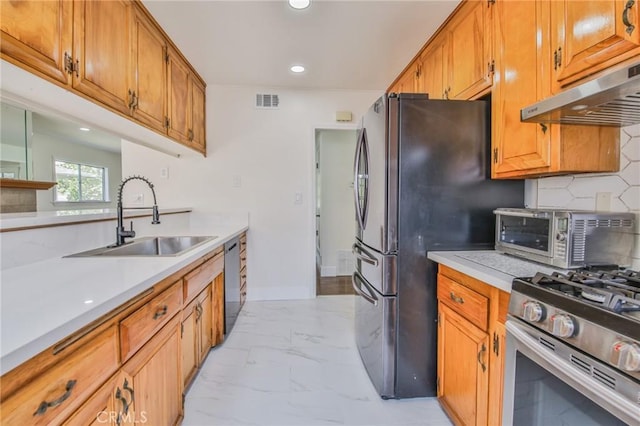 kitchen featuring marble finish floor, a toaster, under cabinet range hood, a sink, and stainless steel appliances