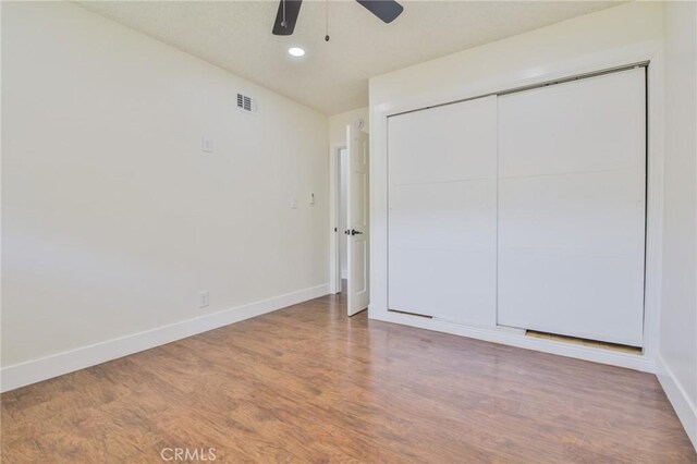 unfurnished bedroom with visible vents, a closet, wood finished floors, baseboards, and a ceiling fan