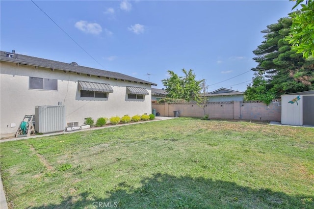 view of yard featuring an outbuilding, central AC unit, a fenced backyard, and a storage unit