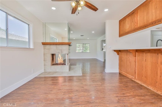 unfurnished living room with ceiling fan, wood finished floors, a tile fireplace, baseboards, and recessed lighting