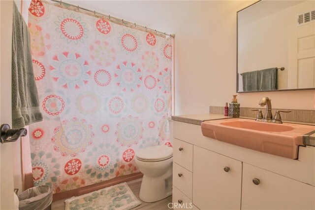 bathroom with vanity, toilet, wood finished floors, and visible vents