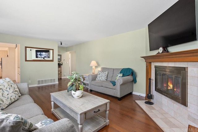 living room featuring baseboards, a tile fireplace, wood finished floors, and visible vents