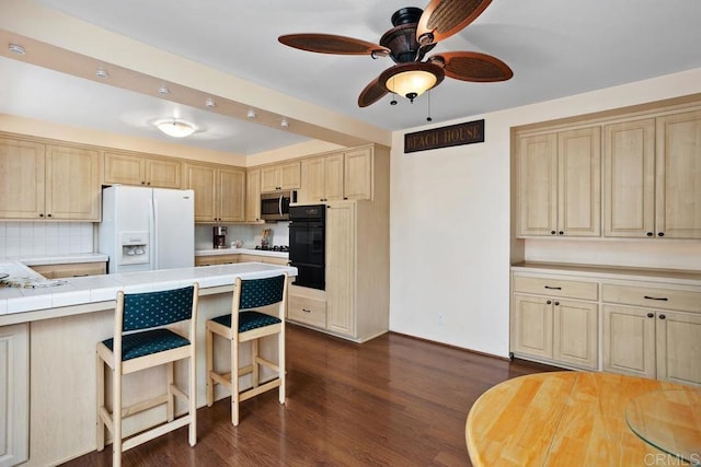 kitchen featuring light brown cabinetry, ceiling fan, white refrigerator with ice dispenser, dark wood-style floors, and stainless steel microwave