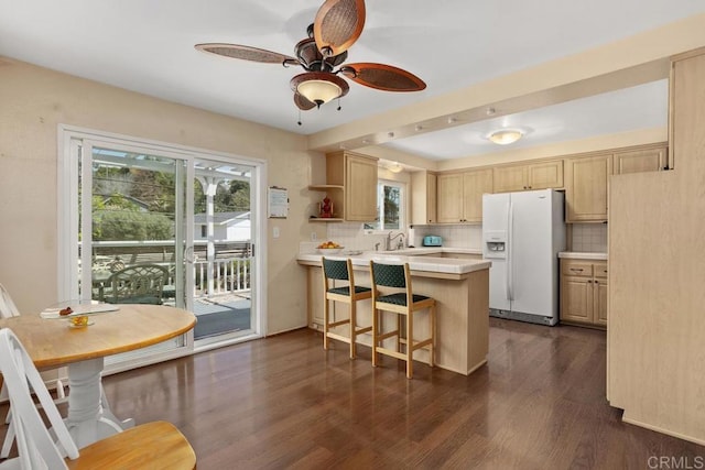 kitchen with backsplash, a peninsula, plenty of natural light, and white fridge with ice dispenser