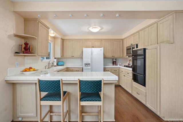 kitchen featuring backsplash, a peninsula, black appliances, and light brown cabinets