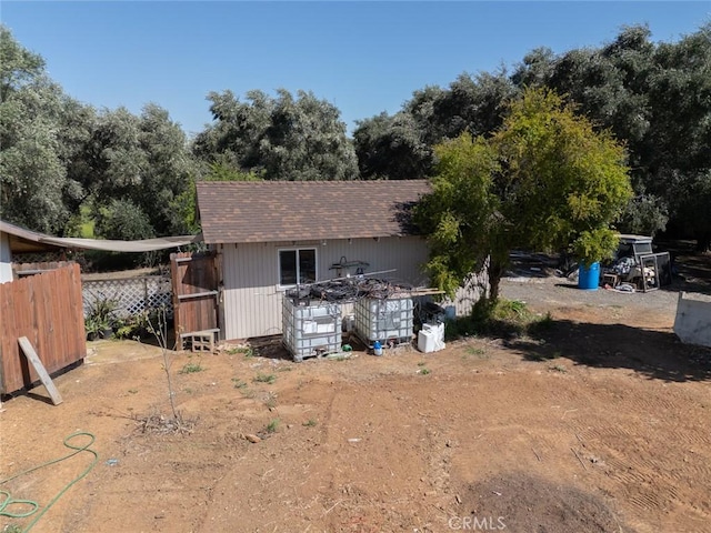 back of house with fence, an outdoor structure, and roof with shingles