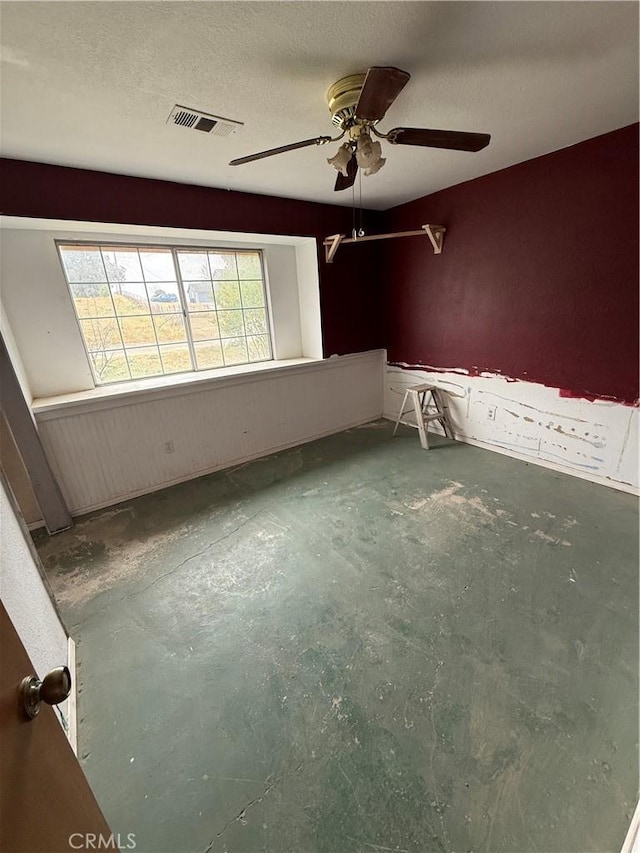 empty room featuring visible vents, a ceiling fan, and unfinished concrete floors