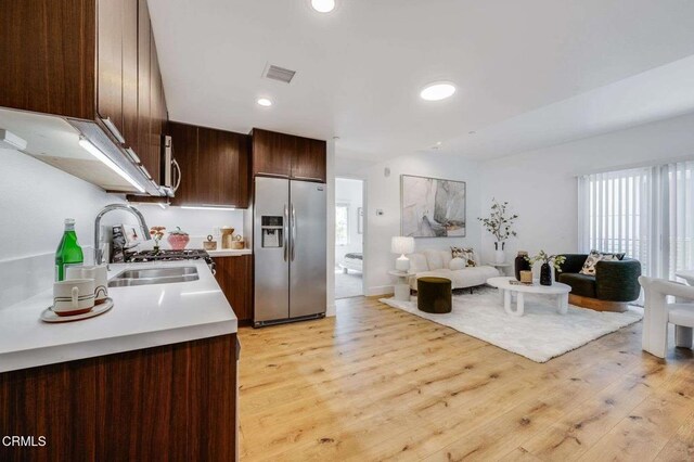 kitchen with dark brown cabinetry, appliances with stainless steel finishes, light countertops, open floor plan, and light wood-type flooring