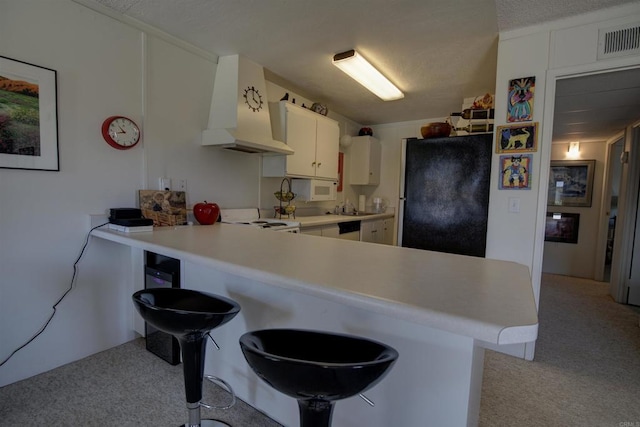 kitchen featuring visible vents, freestanding refrigerator, a peninsula, light carpet, and custom range hood