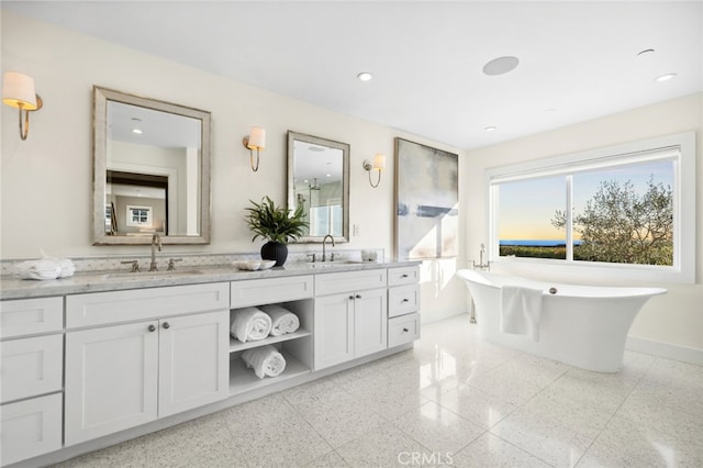 bathroom featuring baseboards, double vanity, a freestanding tub, and a sink