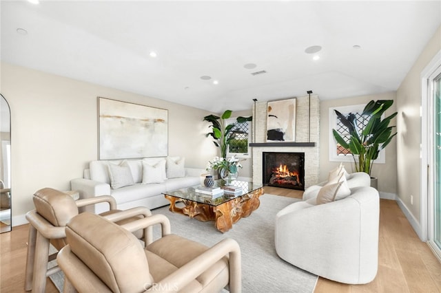 living room with a large fireplace, visible vents, light wood finished floors, and a wealth of natural light