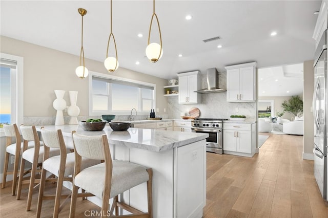 kitchen with wall chimney range hood, white cabinets, stainless steel appliances, and visible vents