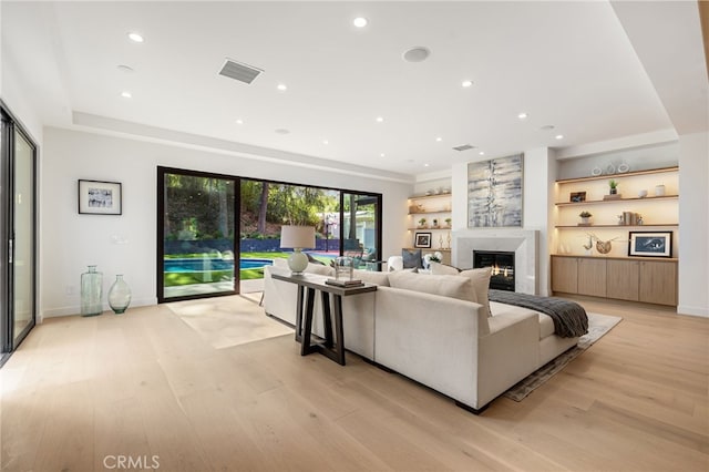 living room featuring visible vents, recessed lighting, light wood finished floors, and a warm lit fireplace