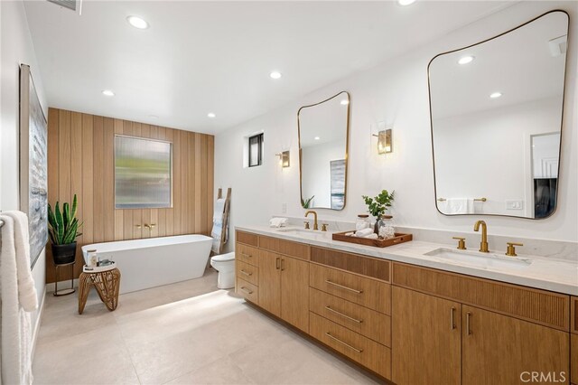 bathroom with a sink, double vanity, wood walls, recessed lighting, and a soaking tub