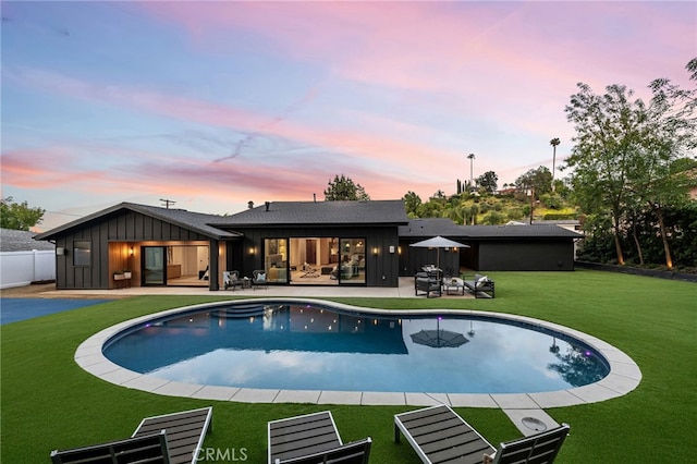 pool at dusk featuring fence, an outdoor pool, an outdoor living space, a patio, and a yard