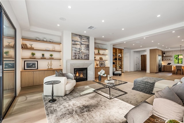 living room featuring recessed lighting, visible vents, a high end fireplace, and light wood-style floors