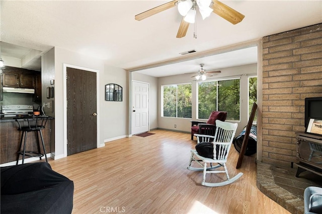 living area featuring visible vents, a wood stove, baseboards, a ceiling fan, and light wood finished floors