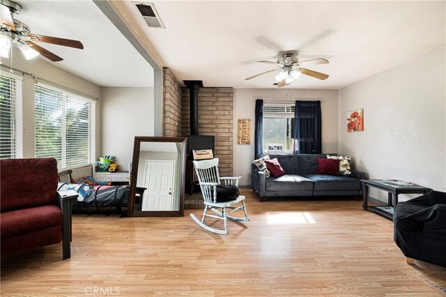 living area featuring visible vents, a ceiling fan, light wood finished floors, and a wood stove