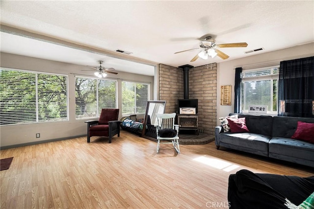 living area with a ceiling fan, visible vents, a wood stove, light wood-type flooring, and baseboards