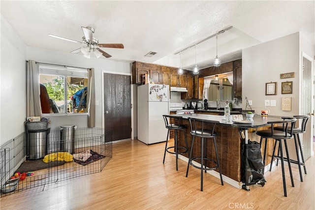 kitchen featuring visible vents, a peninsula, white appliances, ceiling fan, and under cabinet range hood