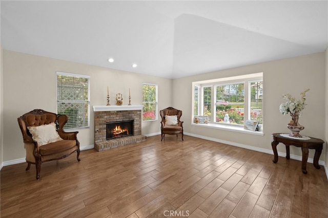 living area featuring baseboards, a brick fireplace, lofted ceiling, and wood finished floors